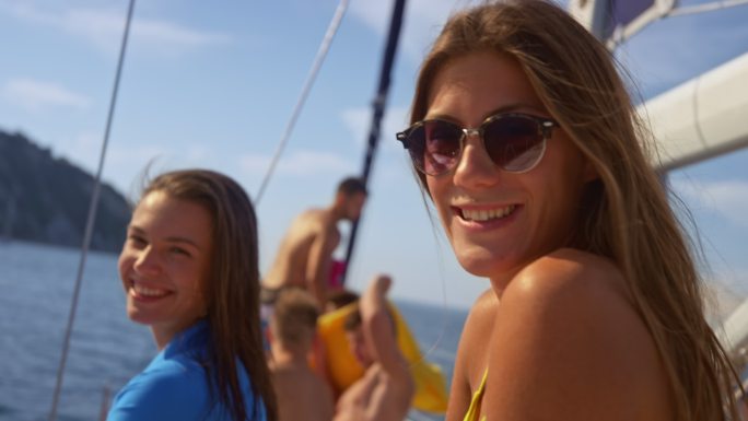 两位年轻女性在阳光下坐在游艇上微笑的肖像
