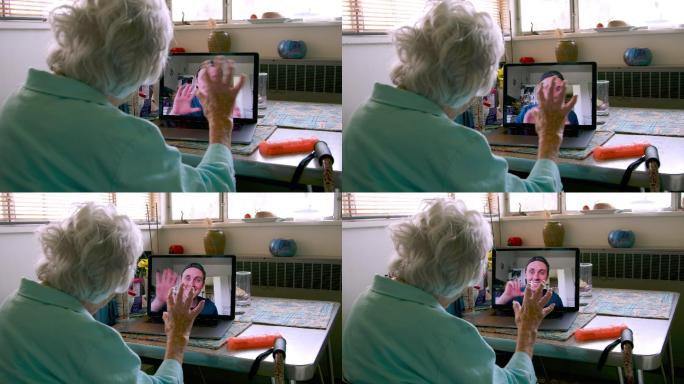 坐在笔记本电脑前的一位100岁的老太太与她的孙子在视频通话中挥手交谈