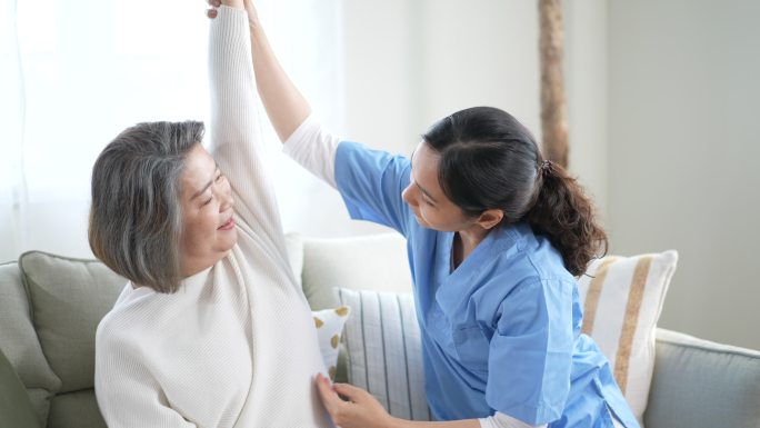 护士理疗为家中伸展手臂的老年妇女提供理疗服务