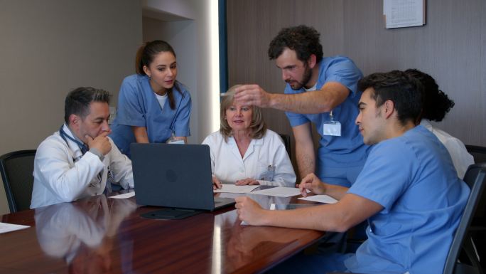 医疗团队在医疗委员会讨论一个病例时，一边看着笔记本电脑上患者的病历表