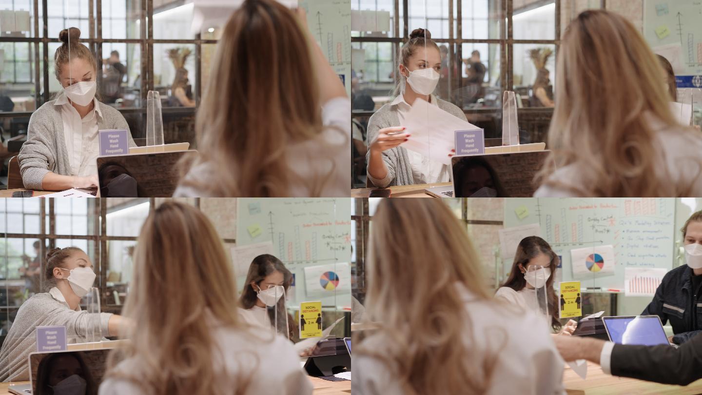 小办公室在2019冠状病毒疾病期间，女商人通过屏幕隔墙给同事发送文件，戴上防护面罩，练习社交距离以确