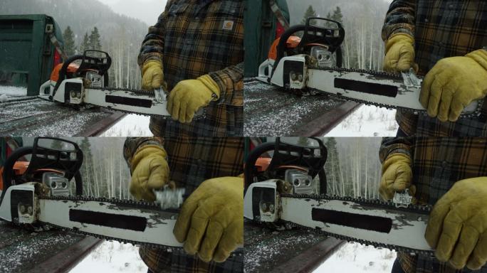 一位30多岁留着胡子的白人男子在森林里的卡车尾门上磨着电锯，这是一个大雪纷飞的冬日，在山里