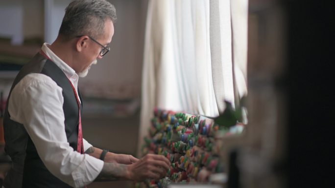 亚裔中国成年男子裁缝师在工作室检查他的织物服装