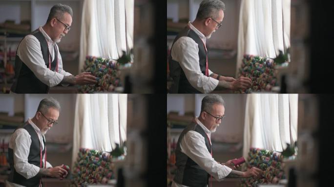 亚裔中国成年男子裁缝师在工作室检查他的织物服装