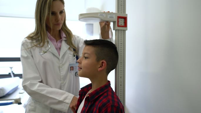 友好的儿科医生在会诊时测量兴奋的小男孩的身高