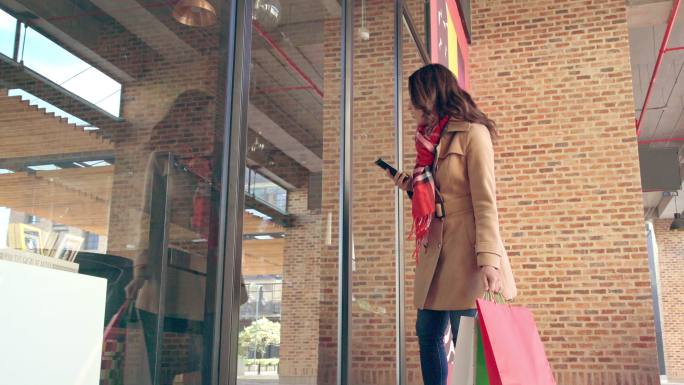 一名拉丁女子手拿手机看着商店橱窗，独自穿过商场