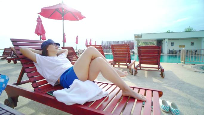 一名亚洲女子躺在游泳池的太阳椅上