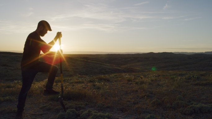 日落时分，一名30多岁的白人男子戴着帽子，在沙漠中用铲子在地上挖洞