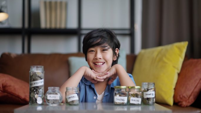 亚洲儿童青少年男性手把硬币放在钱罐里，在家里接受理财教育，微笑的亚洲男孩快乐而自豪地集资回家理财理念