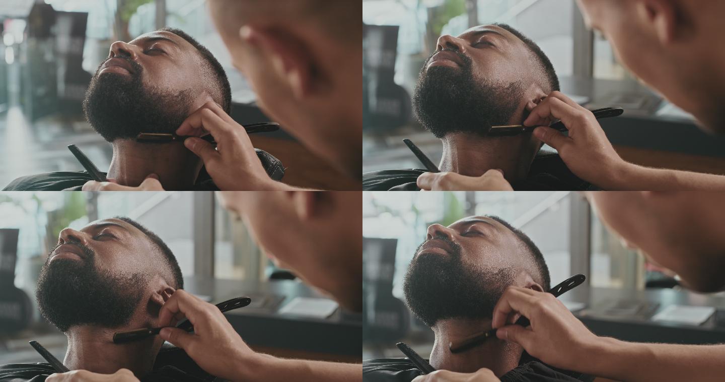 一个英俊的年轻人坐在理发店里，被理发师剃胡子的4k视频片段