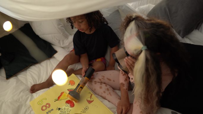 兄弟姐妹们在家里的毯子帐篷里玩耍，其中包括一个患有斑秃症的女孩