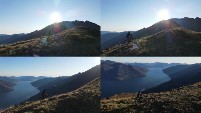 日落时山地摩托车手登上湖面山脊鸟瞰图