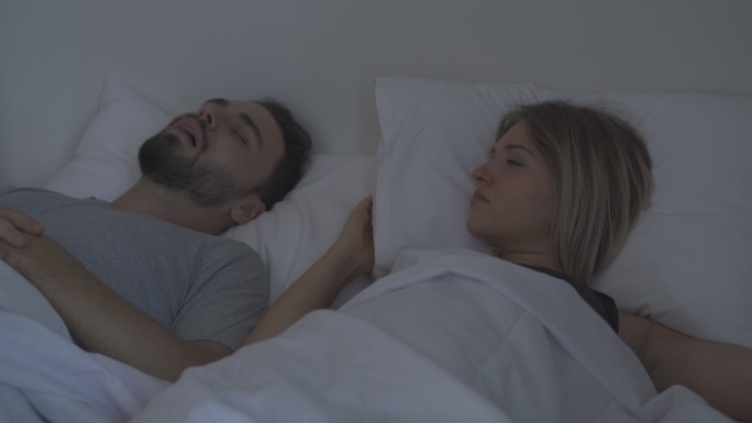 丈夫打鼾，妻子用枕头捂着头。