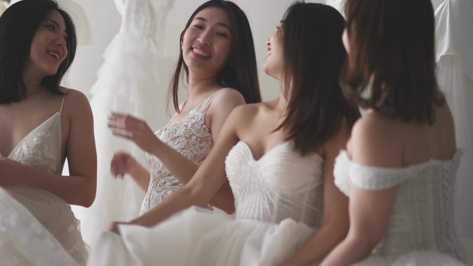 慢镜头快乐嬉戏的亚洲华人新娘和伴娘在婚纱店试穿婚纱，欢天喜地地共舞