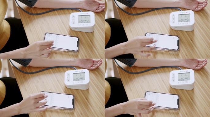 POV：亚洲女性在血压监护仪上自我测量血压和心率，在家中使用智能手机记录数据