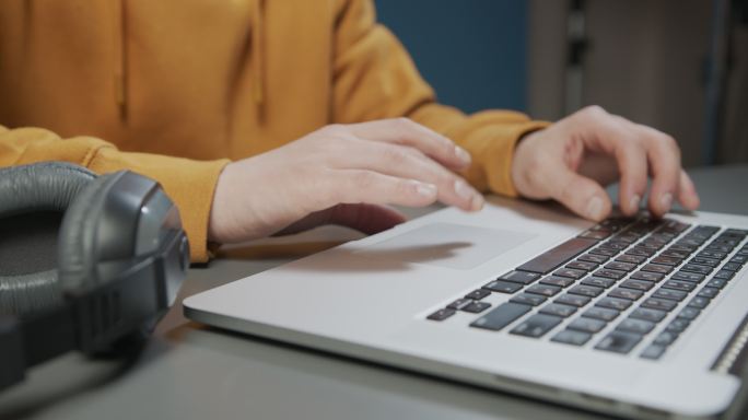 一名男子的手放在桌上，在银色笔记本电脑上打字