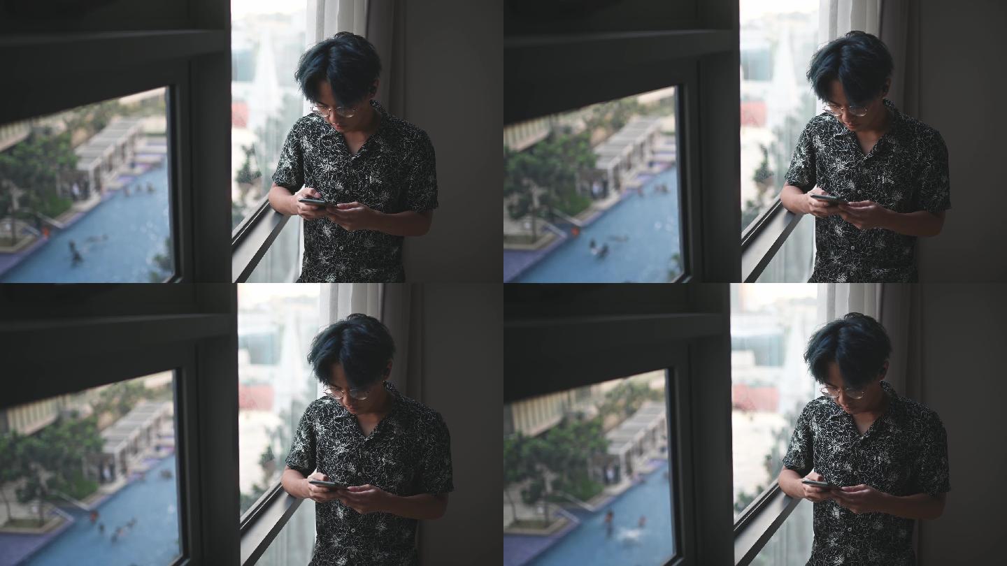 周末，亚裔中国少年倚靠客厅窗户使用智能手机