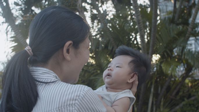 亚洲母亲在夕阳下亲吻她的新生男婴，同时在室外公园放松。