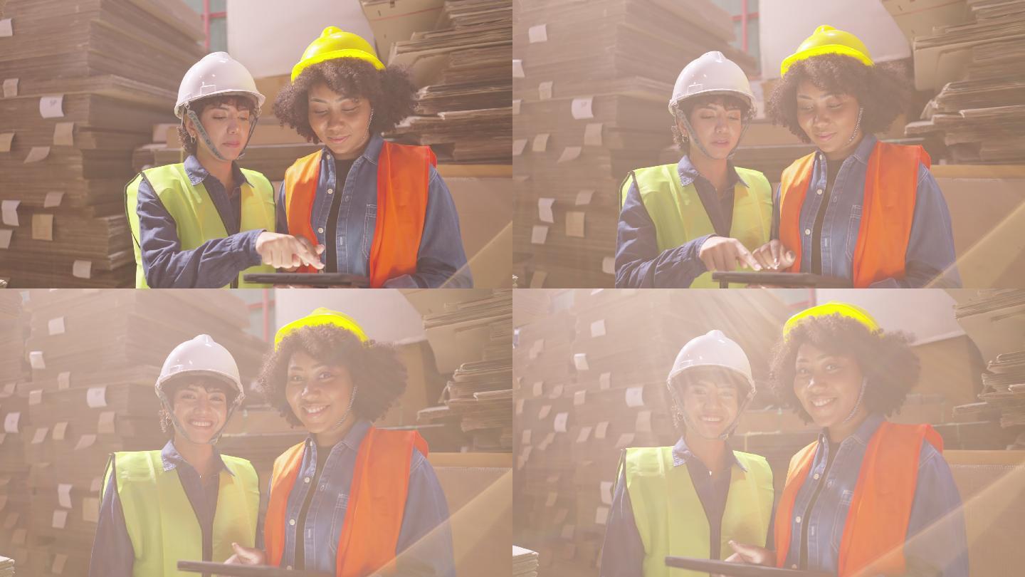 阳光耀斑：在纸包装厂工作的拉丁和非洲女工们穿着安全背心和头盔，使用数码平板电脑和智能手机，微笑着看着