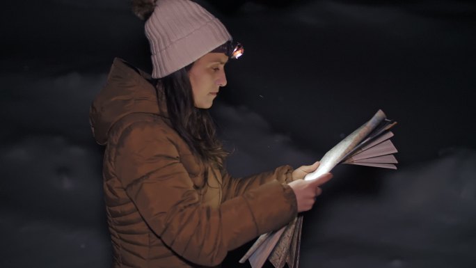 冬季旅行者在夜间看地图，一位年轻女性游客在冬季山脉中行走的中景照片，肖像，旅游，探险，旅游，决心，运