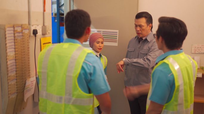亚洲蓝领工人与工厂主管在时钟考勤机旁交谈