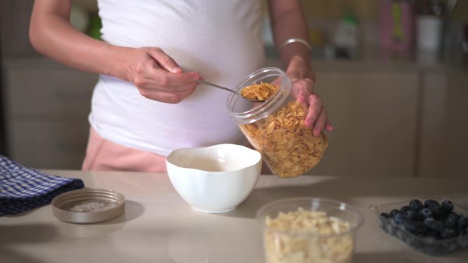 孕妇在家里做早餐玉米片，在厨房里添加配料。制作富含纤维和营养的健康有机膳食