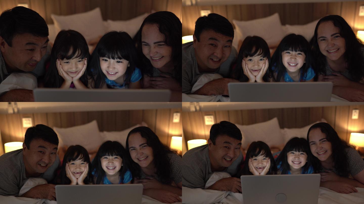 一家人躺在床上看家里笔记本电脑上的东西的肖像