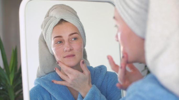 女人在脸上涂护肤霜照镜子