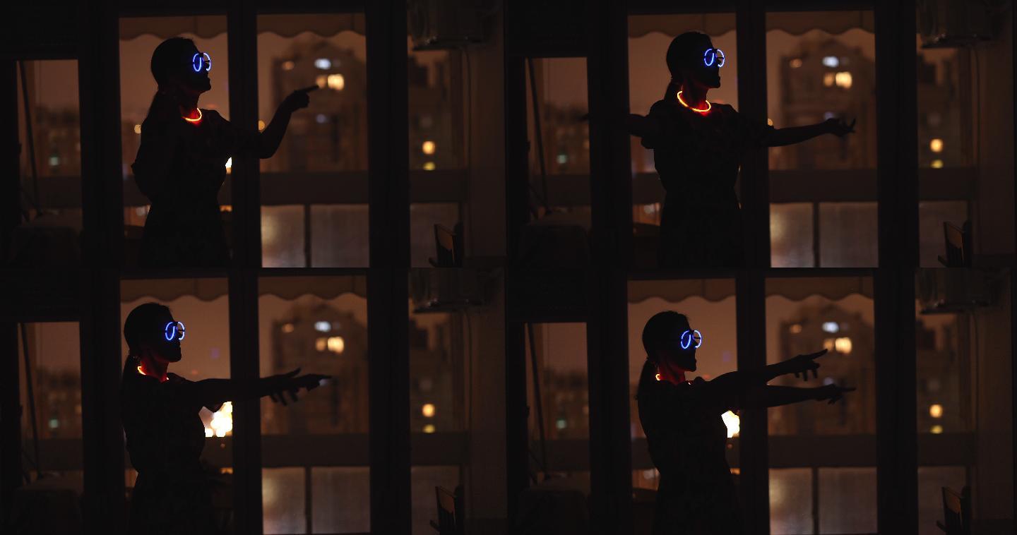 戴着霓虹眼镜和手镯的女人在窗户前的暗室里跳舞