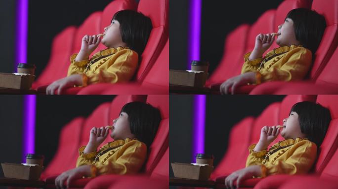 侧视亚裔中国女孩一边吃薯条一边独自在电影院看电影