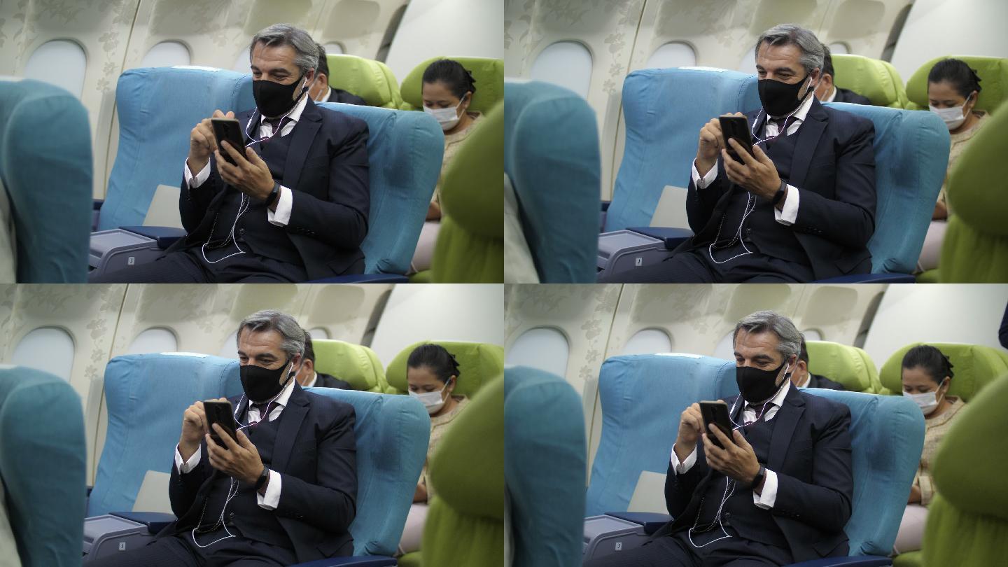 带着防护面罩的商人在出国旅行期间在飞机上使用手机。乘客们用电话消磨无聊的时间。新的正常旅行。