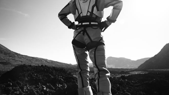 在月球上散步。女宇航员探索灰色山脉。看着干燥的火山景观。特写镜头