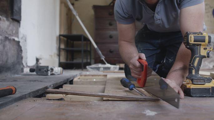 男建筑工人在地板上使用锯子