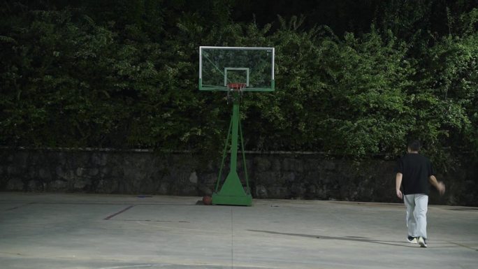夜晚一个人在农村环境的篮球场上投篮上篮