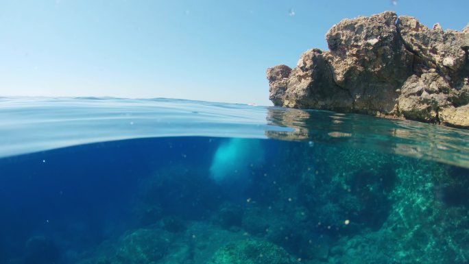 中景：克罗地亚亚得里亚海，身穿比基尼的年轻女子从岩石上跳入阳光明媚的海洋