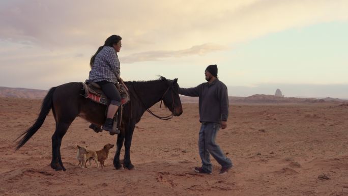 美丽的夕阳下，年轻的纳瓦霍女孩在亚利桑那州纪念碑谷部落公园抚摸着她骑的马