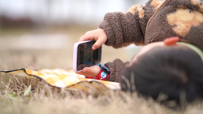 儿童侧躺在草地上拨动手机画面