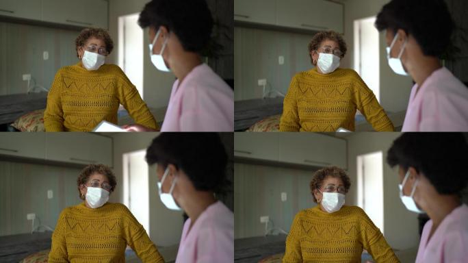家访期间，医生在卧室与老年患者交谈-戴上防护面罩