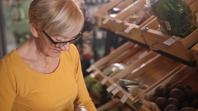 一位上了年纪的妇女在有机食品店购买食品的侧视图。