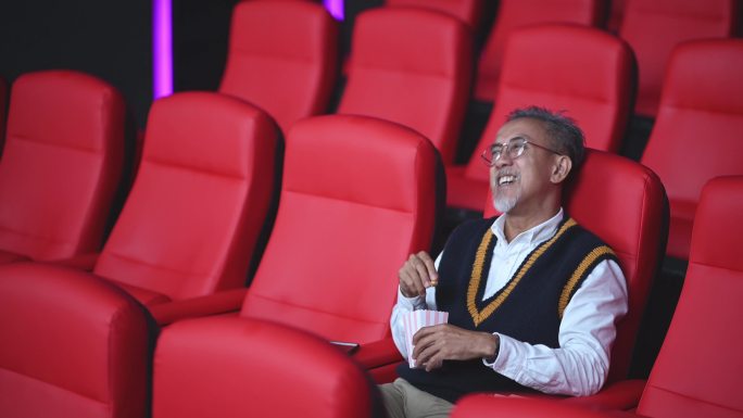 亚裔华人活跃老人独自在电影院看电影，一边吃零食
