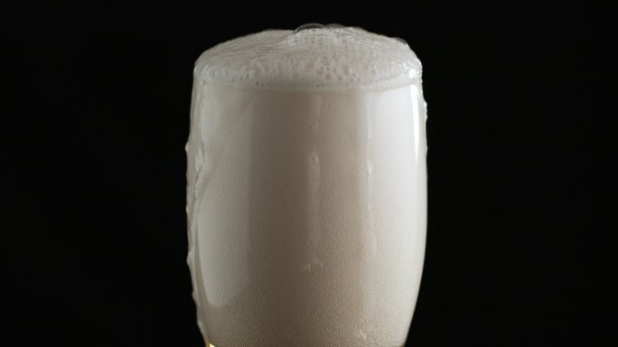 啤酒泡沫流到玻璃边缘，然后在黑色背景上沿玻璃侧面向下流动