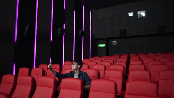 中国亚裔年轻人独自在电影院看电影时用手机自拍