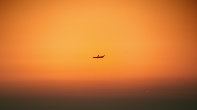 黄昏时分在橙色天空中飞过的飞机