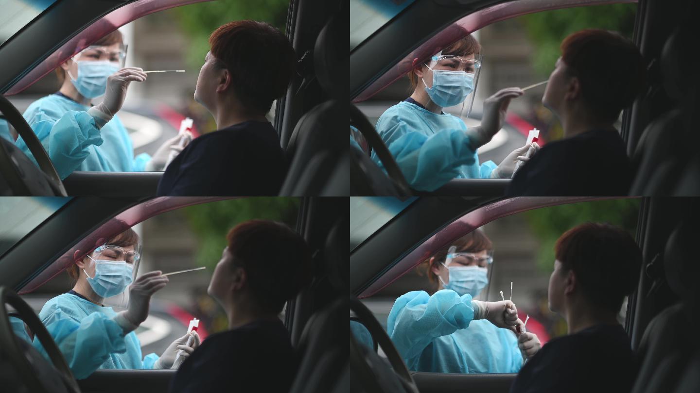 在停车场的室外，亚裔中国女医生带着PPE从患者冠状病毒试验中取鼻拭子。防护套间的医务人员正在用拭子进