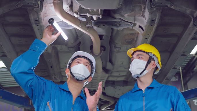 两名亚裔汽车技师戴着面具，在汽车修理厂工作。车辆服务经理团队男员工查看车辆状况，检查和维护，以便在车