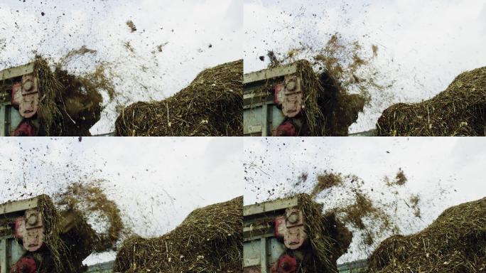在一个多云的日子里，一个肥料撒布机将肥料喷洒到农场的一个大堆中的慢镜头