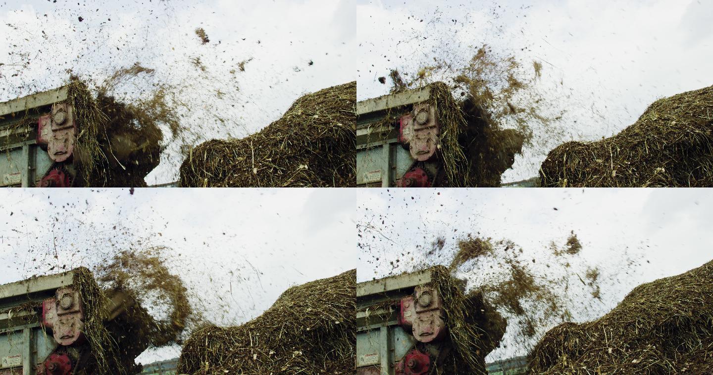 在一个多云的日子里，一个肥料撒布机将肥料喷洒到农场的一个大堆中的慢镜头