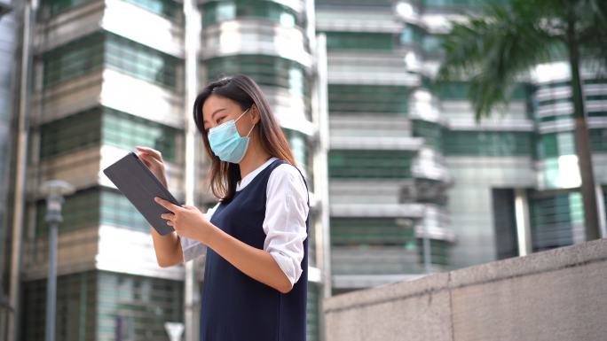 年轻的亚洲女性戴着防护面罩，在户外使用数码平板电脑