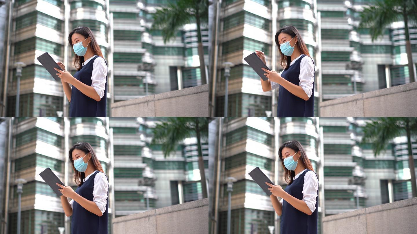年轻的亚洲女性戴着防护面罩，在户外使用数码平板电脑