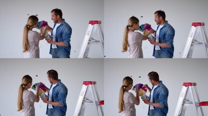 一对幸福的夫妇在家里选择一种颜色，同时看着一个色样和他们要粉刷的墙壁
